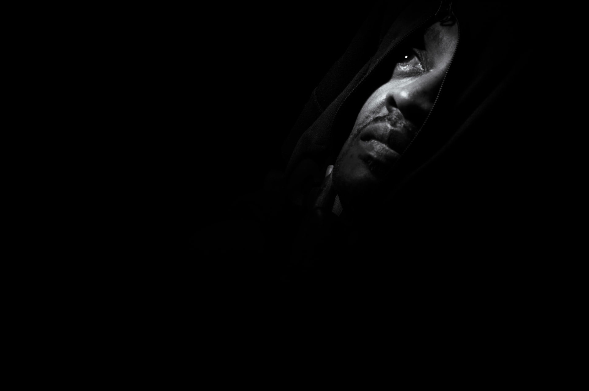 Editorial photography — Quiet Resilience personal project, low-key black and white portrait of a hooded man looking upward